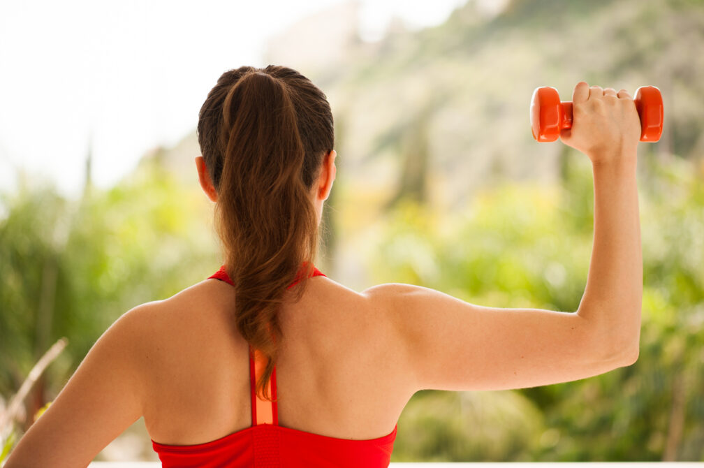 Young athletic woman exercising on verandah: overhead press for upper body strength